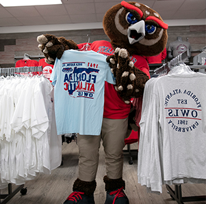 FAU mascot, Owlsley, holding up an FAU shirt in the bookstore